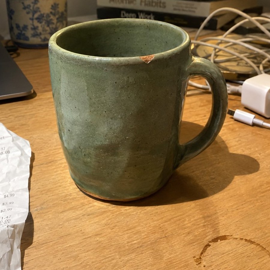 A handmade mug photographed on a cluttered desk under harsh lamp light